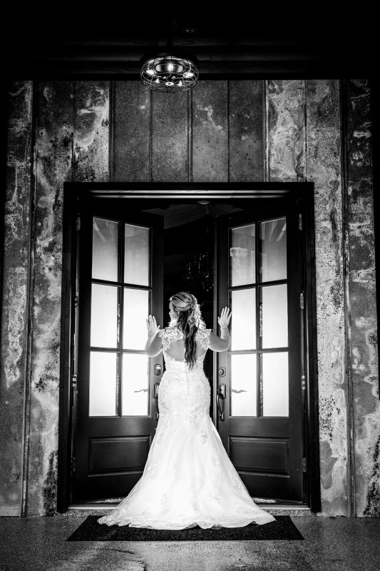 Bride in a lace-back gown framed by open French doors in dramatic black and white at The Lonesome Dove